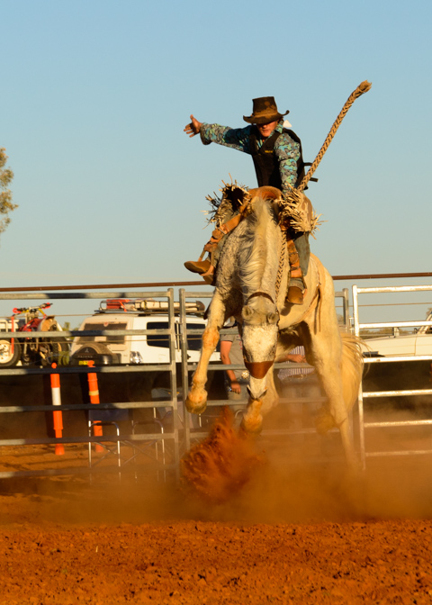 A bronco kicks up red dust as it bucks during a rodeo in Windorah, Queensland, Australia, while a rider grips the reins mid-ride.