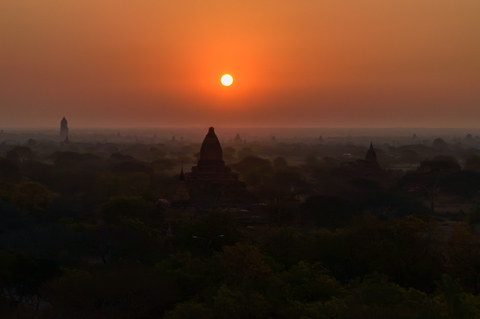 The sun rises through morning haze over the silhouetted temples and pagodas of Bagan, Myanmar.