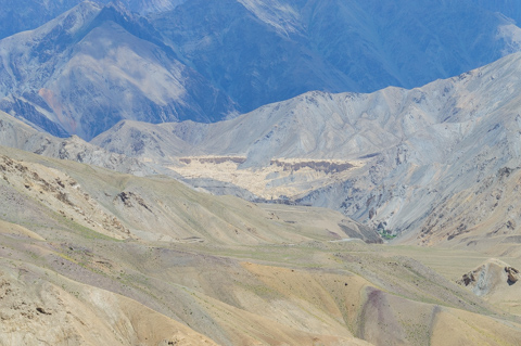 Layered, barren mountains in Ladakh form a vast high-altitude landscape, with pale ridgelines and deep blue shadows receding into the distance.