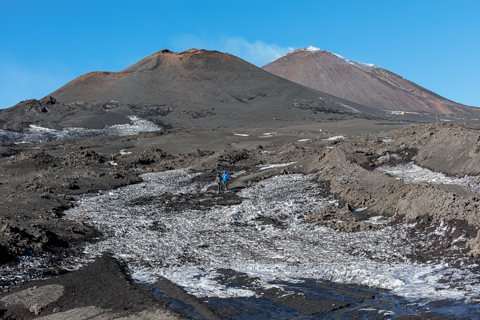 Two hikers cross frozen snowfields and dark volcanic ash on Mount Etna’s upper slopes before the February summit collapse.