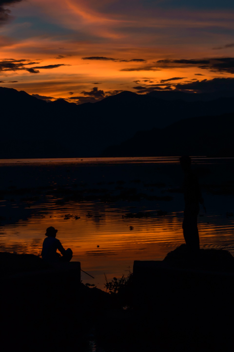 Two silhouettes of men fishing during sunset at Fewa Tal, Lakeside Pokhara, Nepal