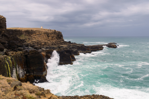 Waves crash against rugged cliffs at Slope Point, with the Southern Ocean stretching toward the horizon under an overcast sky.