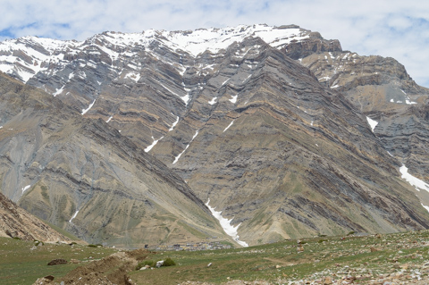 Remote Himalayan village of Mudh in Spiti Valley, surrounded by barren mountains and snow-streaked ridgelines under a pale sky.