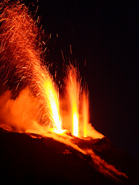 A close-up view of Stromboli Volcano shows bright lava fountains erupting into the night sky, with molten rock spraying upward against a dark, starless backdrop.