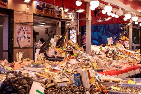 A wide selection of fresh fish and seafood is displayed on ice at a bustling market stall in Palermo, Sicily, Italy, under warm hanging lights.