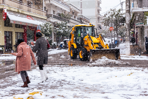 A tractor clears snow from a city street in Athens, Greece, as pedestrians walk through falling snow during a rare winter storm.