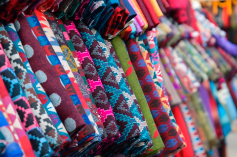 Bolts of brightly colored textiles with patterned designs hang side by side at a street market in Kathmandu, Nepal.