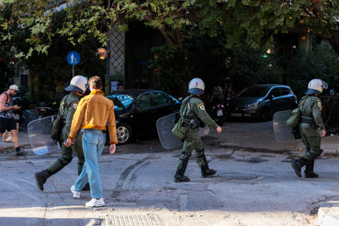 A lone bold pedestrian walks toward a line of riot police carrying shields during a security operation in the Exarcheia neighborhood of Athens, Greece.